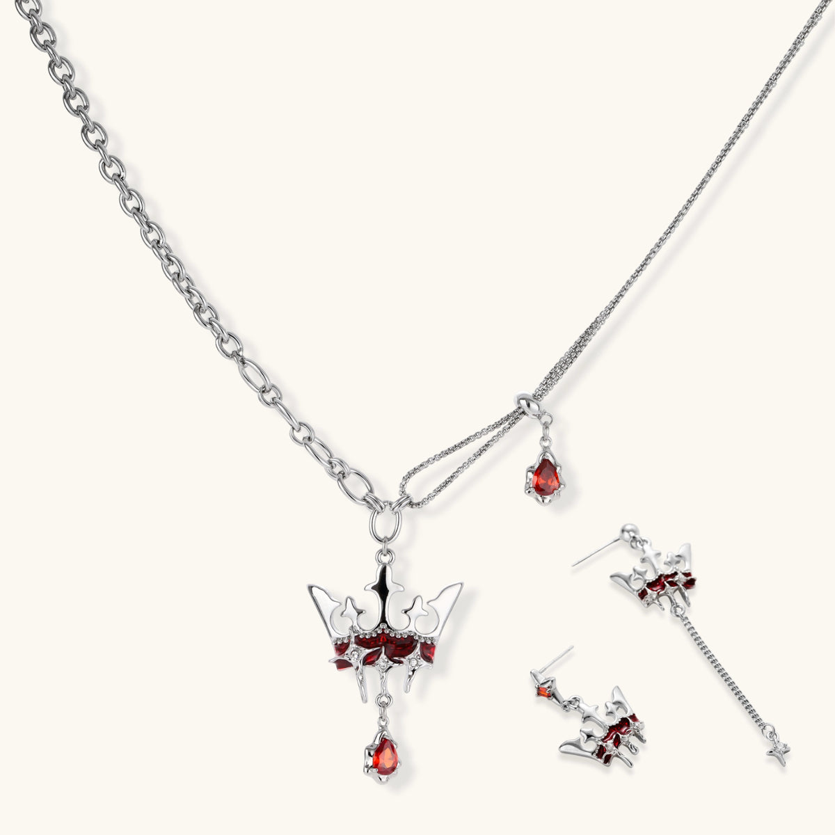 Silver-tone crown pendant with red zirconia stones and matching asymmetrical earrings on cream background