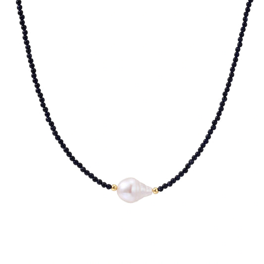 Delicate necklace with black blue sandstone beads and baroque pearl center on white background with gold accents.