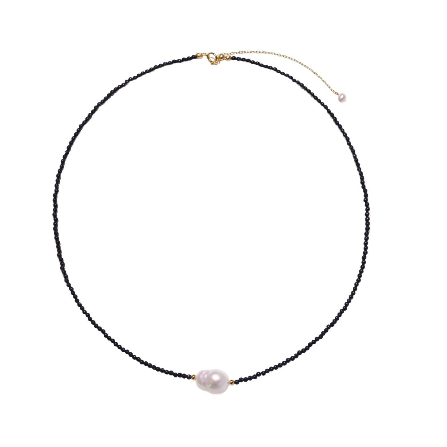 Delicate necklace with black blue sandstone beads and baroque pearl center on white background with gold accents.