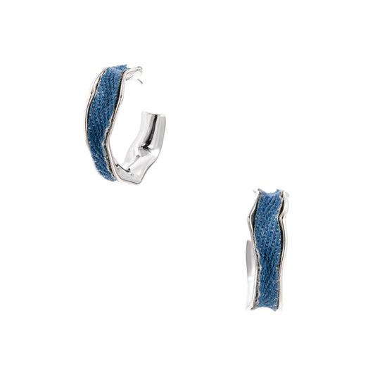 Silver huggie hoops with blue denim fabric inlay strip and polished white gold plated finish on cream background.