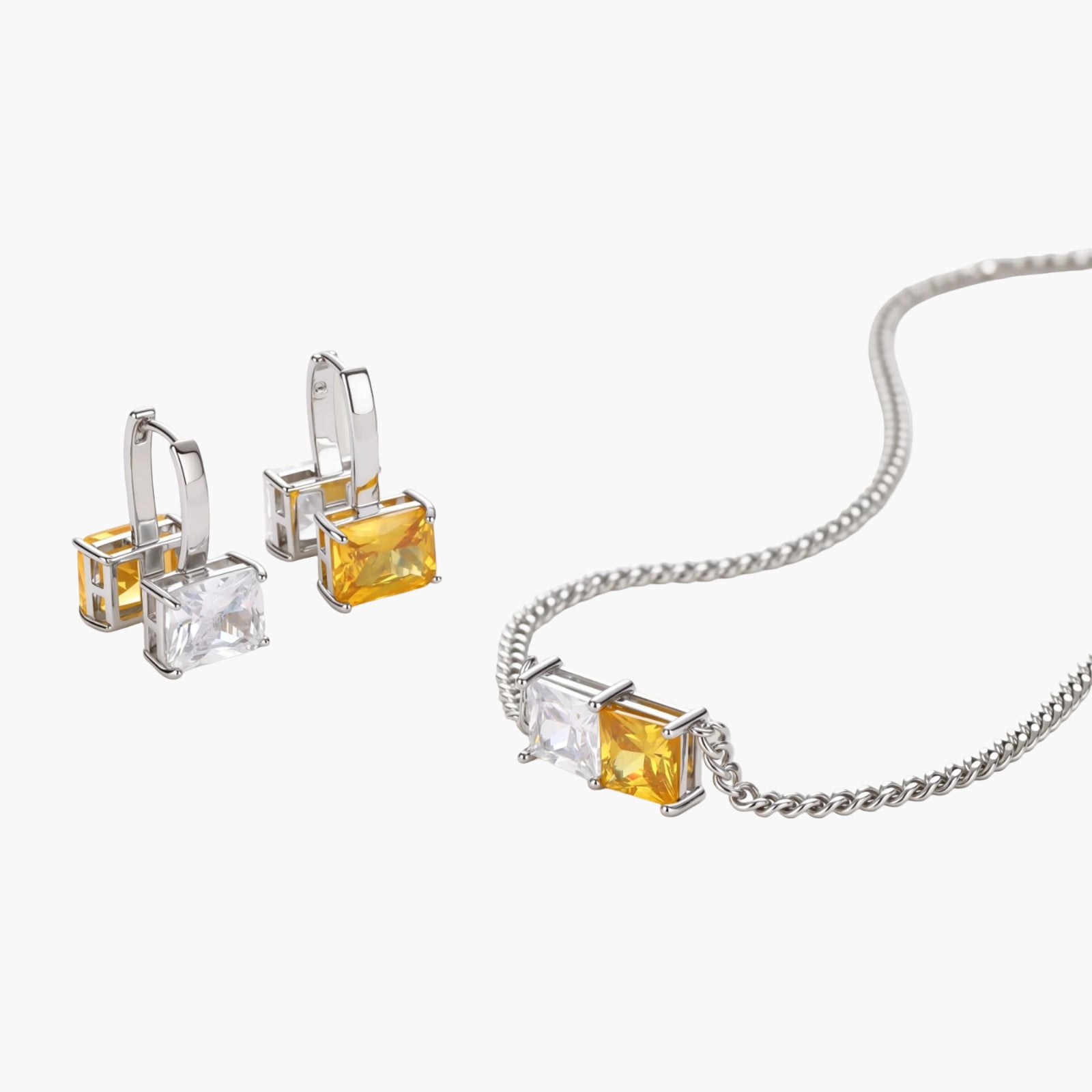 Silver curb-chain necklace and hoop drop earrings set with paired yellow and clear square zirconia stones.